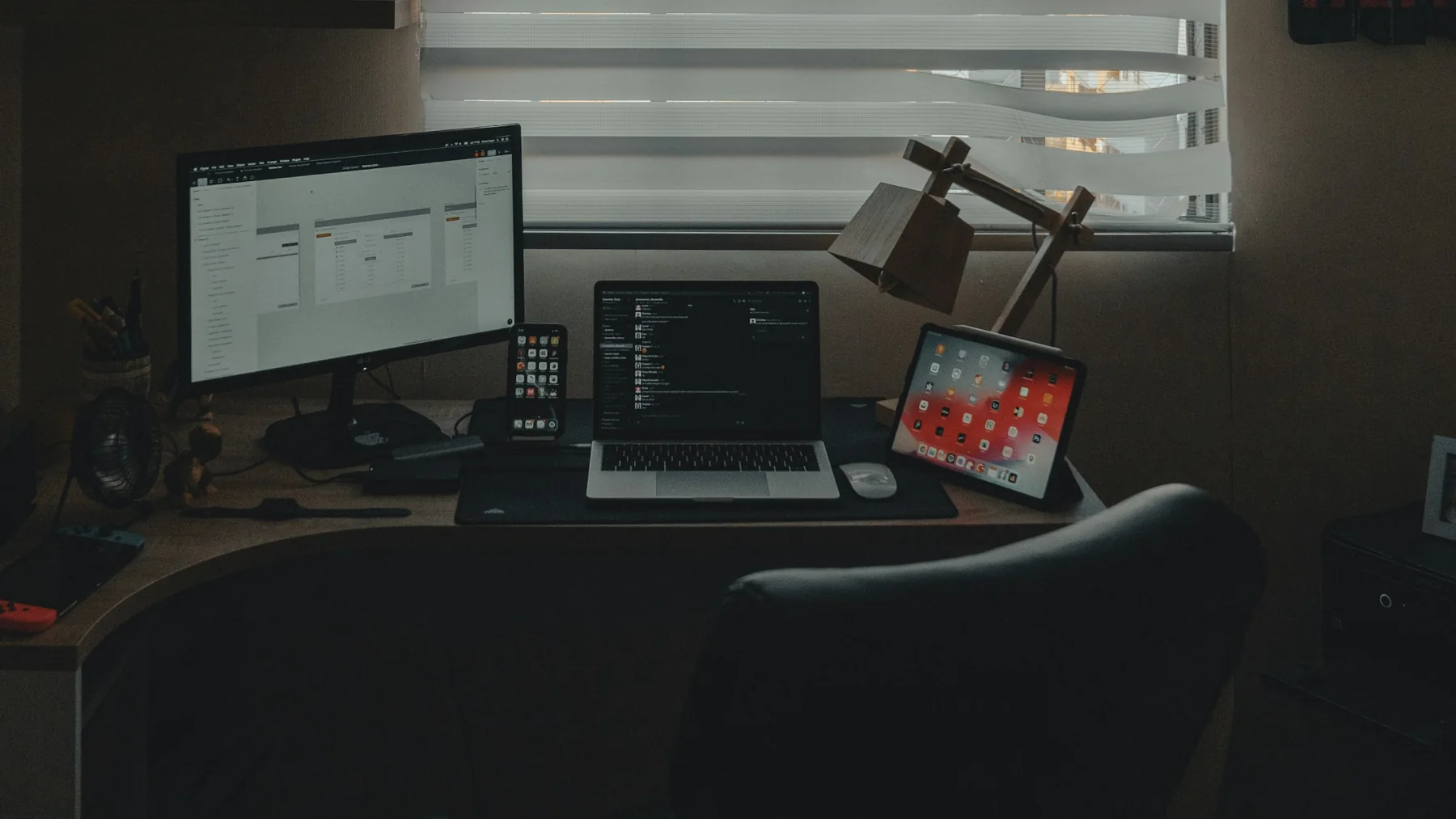 A widescreen monitor displaying website interface layouts alongside a laptop and tablet in a dimly lit workspace, photographed by Alvaro Reyes.